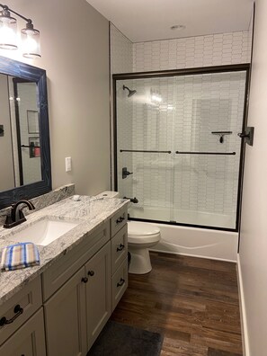 Un baño con ducha envuelta en vidrio, un lavamanos con encimera de mármol y un inodoro.