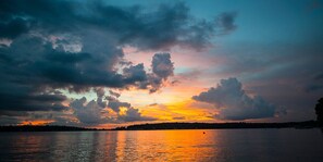 Un atardecer sobre un cuerpo de agua tranquilo, con el perfil silueteado de una costa lejana.