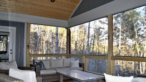 A cozy indoor seating area with wicker furniture and large windows overlooking a forest.