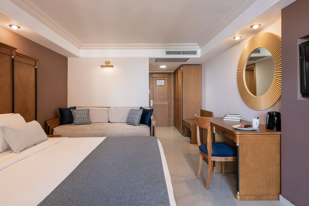 A hotel room with a bed, a desk, a chair, a mirror, and a wardrobe.