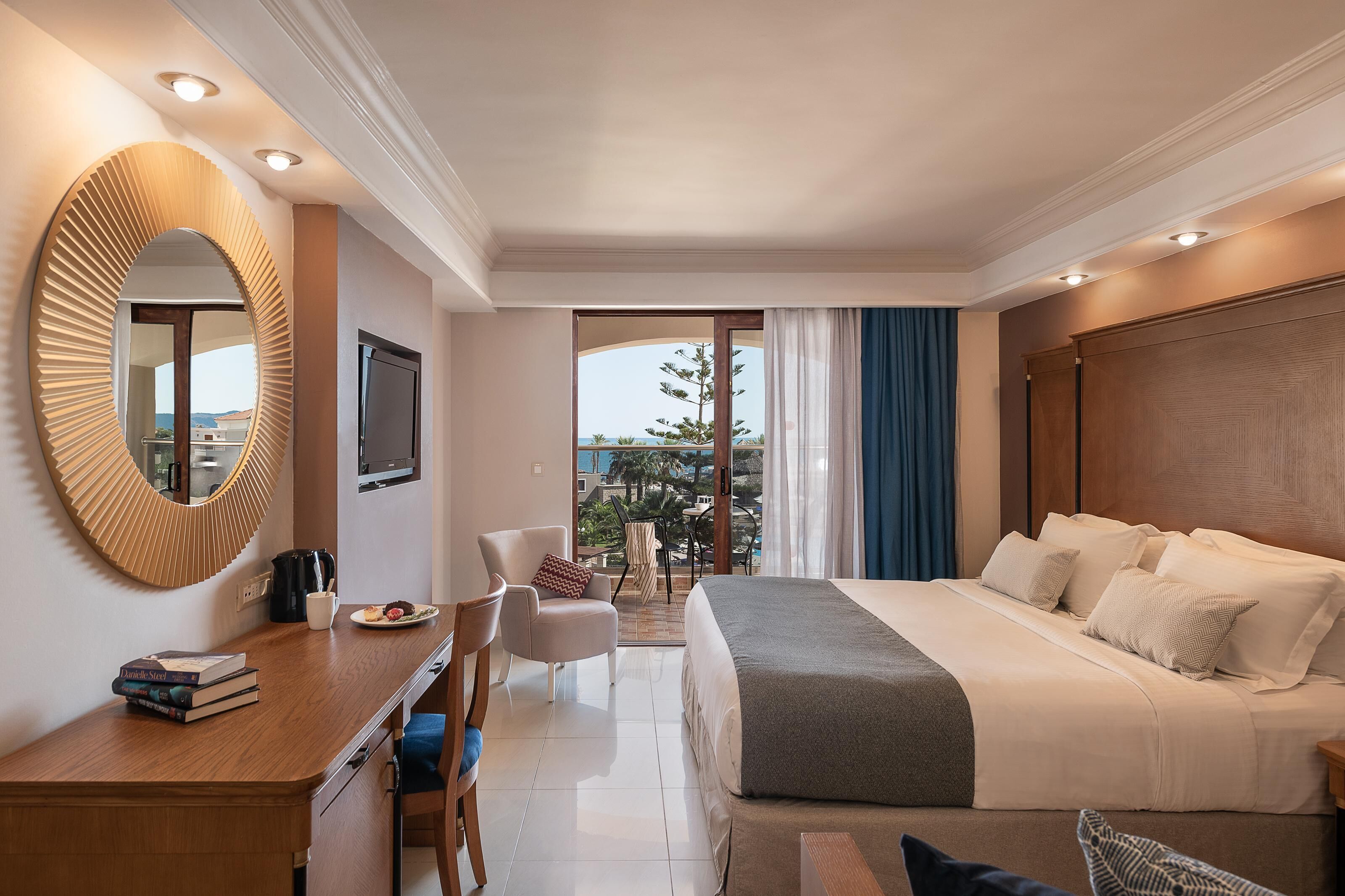 A hotel room with a large bed, a desk with a mirror, a chair, and a view of the outdoors.