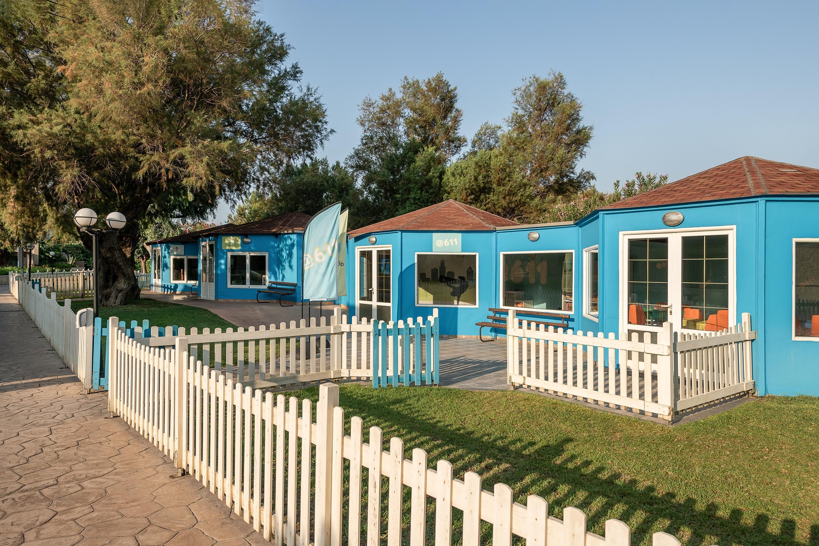 A row of blue buildings with white picket fences, each with a door and windows.