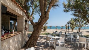 An outdoor seating area with tables and chairs, a bar, and a view of the sea. - Caldera Creta Paradise (Platanias)