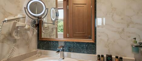 A bathroom with a marble sink, two round mirrors, a hairdryer, and toiletries on the counter.