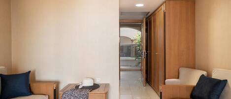 A hotel room with two sofas, a small table with a hat and a patterned cloth, and a wooden wardrobe.