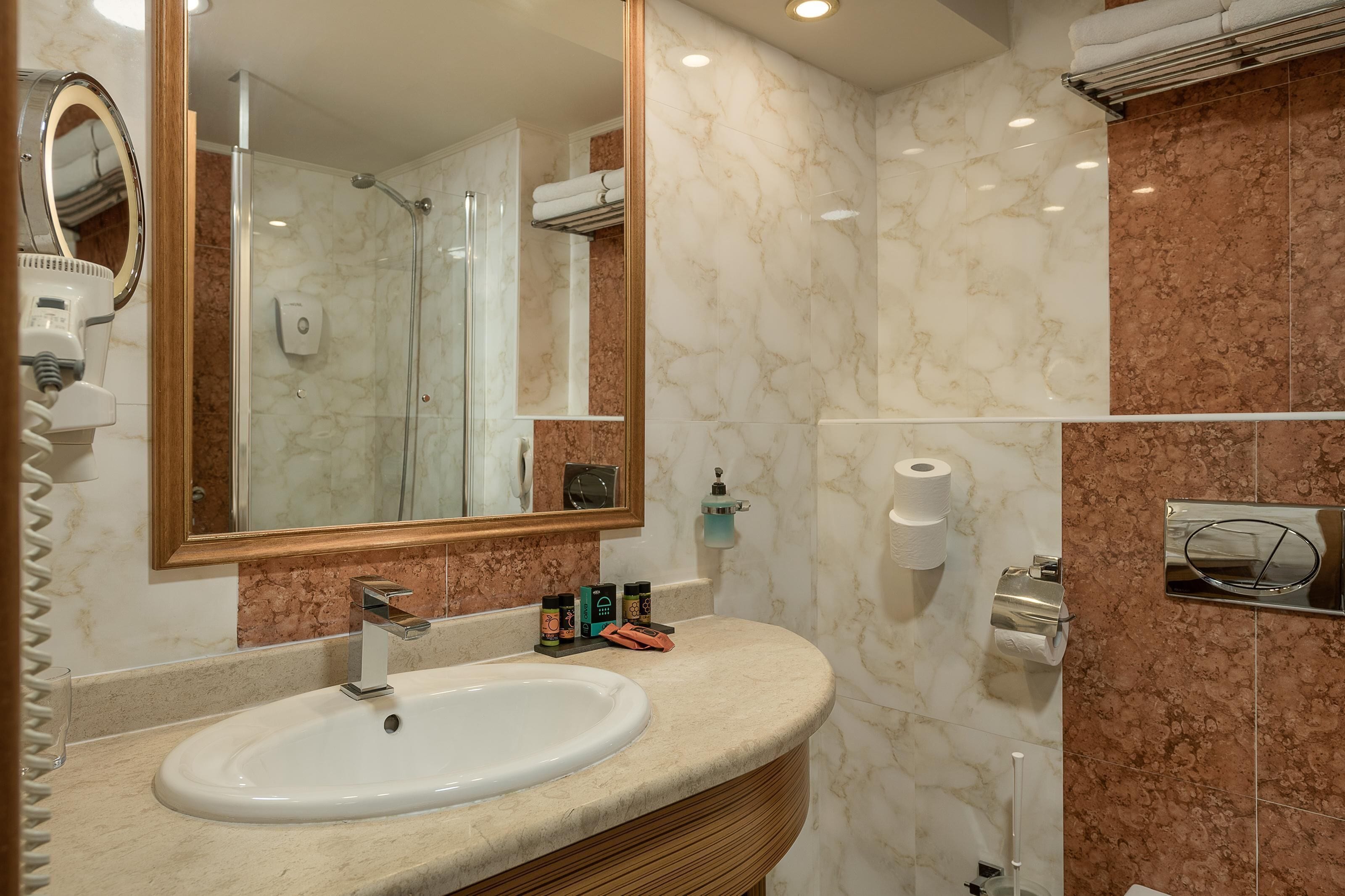 A bathroom with a marble sink, a large mirror, a glass-enclosed shower, and a towel rack.