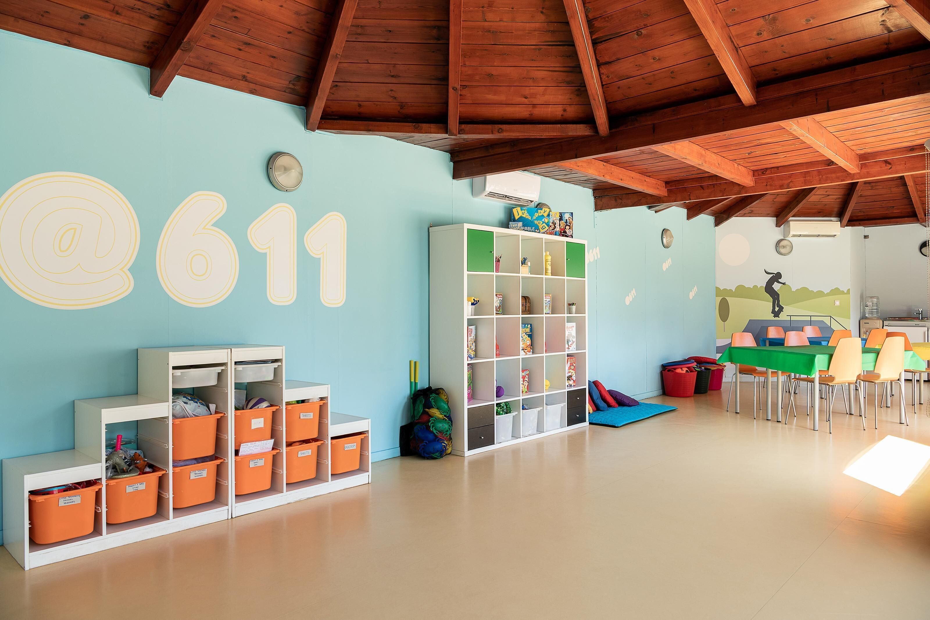 A spacious room with a high ceiling, wooden beams, a large white shelving unit, and a colorful mural on the wall.