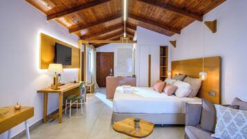 A modern hotel room with a wooden ceiling, a bed with pillows, a sofa, a desk with a lamp, and a chair.