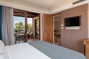 A hotel room with a bed, a television, a sliding glass door to an outdoor area with a table and chairs, and a wooden door.