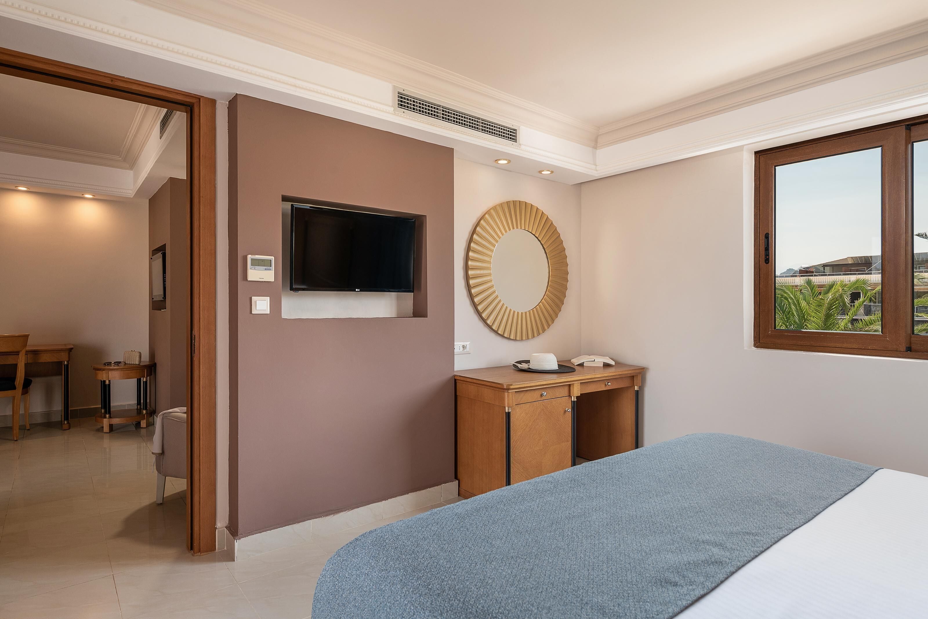 Habitación de hotel con cama, escritorio, televisor, espejo y ventana con vistas.
