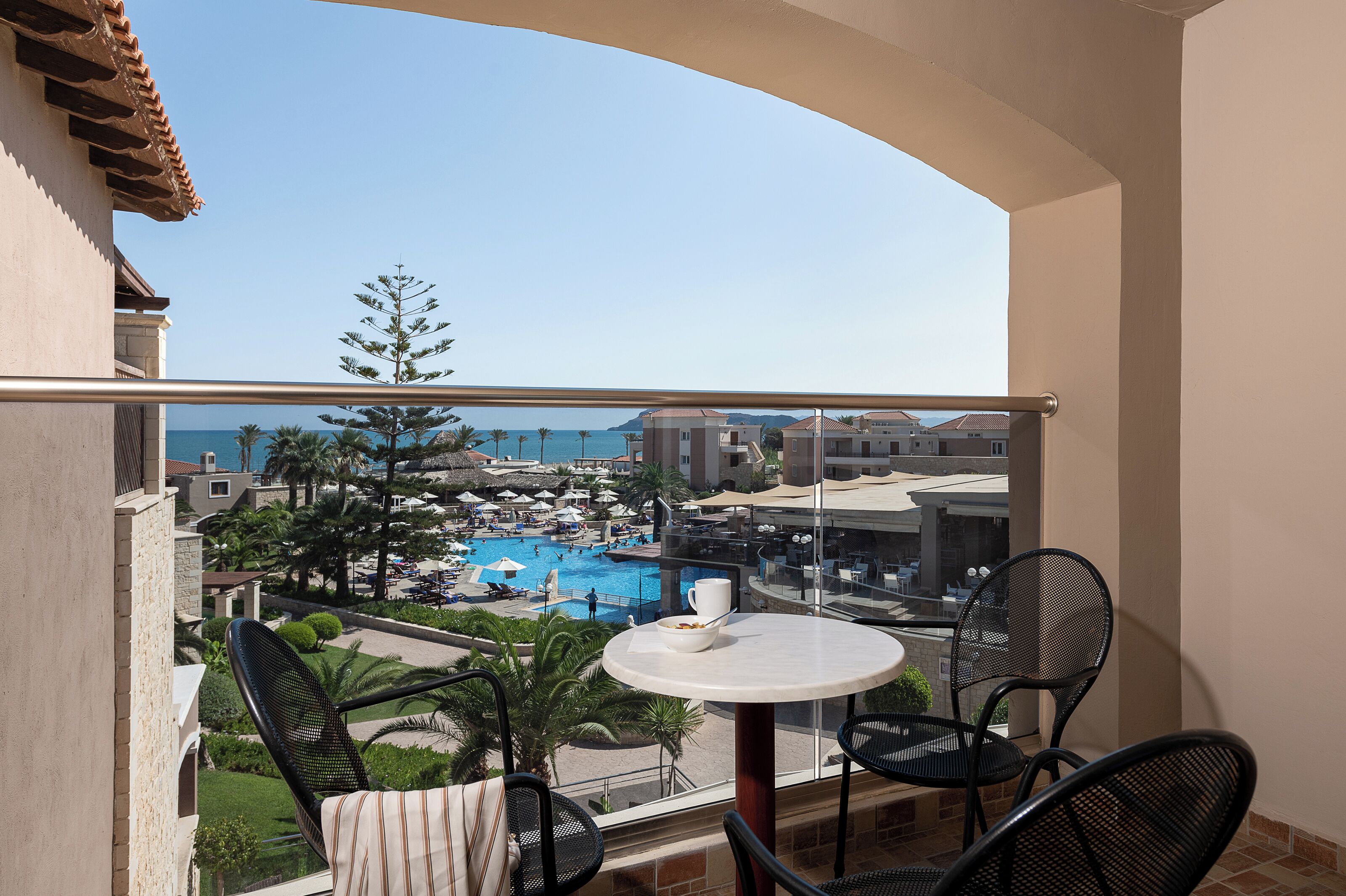 A balcony with a view of a pool and resort area, including lounge chairs and a table.