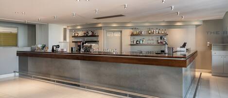 A modern bar area with a long counter, shelves with bottles, and a clean, tiled floor.