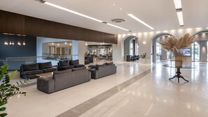 A spacious lobby with a large sectional sofa, a glass railing, and a modern chandelier. - Caldera Creta Paradise (Platanias)