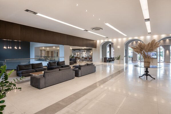 A spacious lobby with a large sectional sofa, a glass railing, and a modern chandelier. - Caldera Creta Paradise (Platanias)