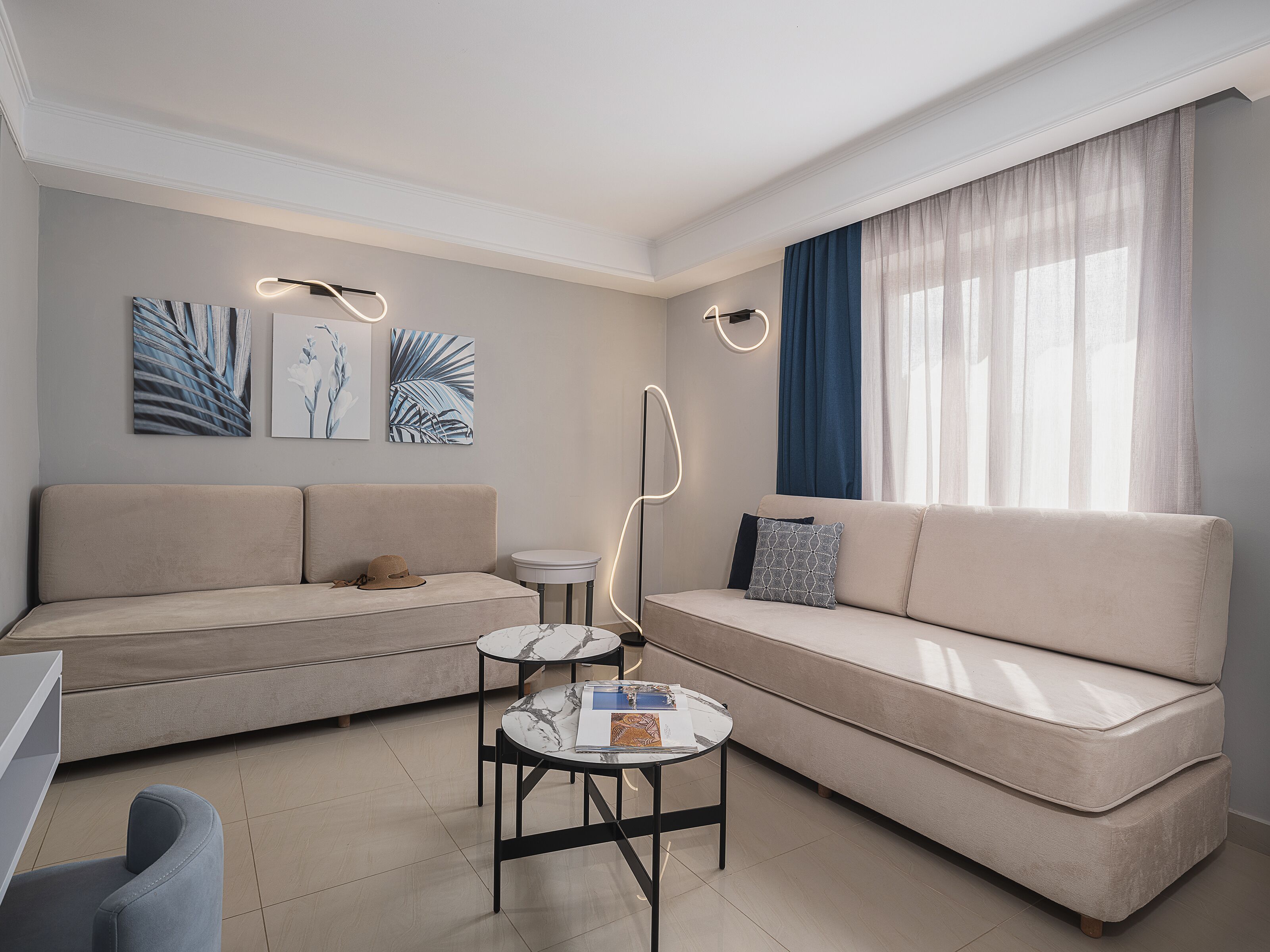 Una sala de estar moderna con un sofá beige, una mesita redonda y obras de arte en la pared.