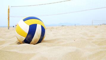A beach volleyball on a sandy surface with a volleyball net in the background.