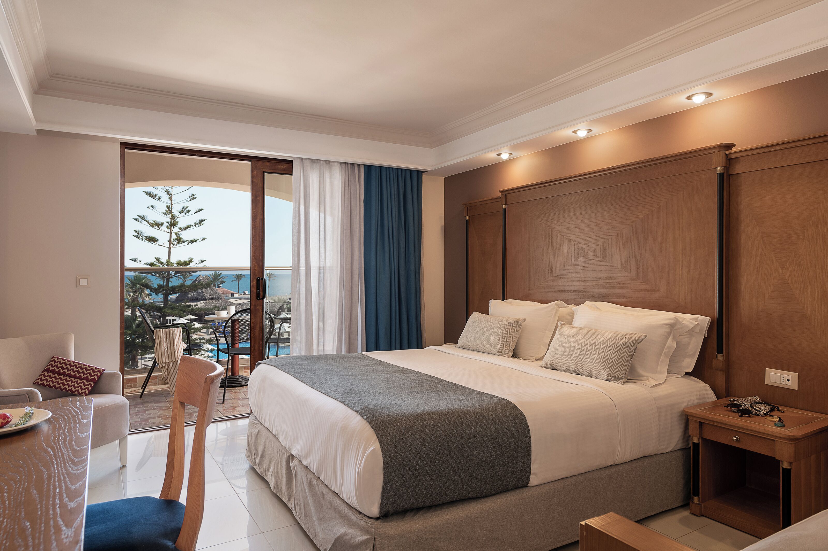 A hotel room with a bed, a desk, a chair, a nightstand, and a view of the outdoors.