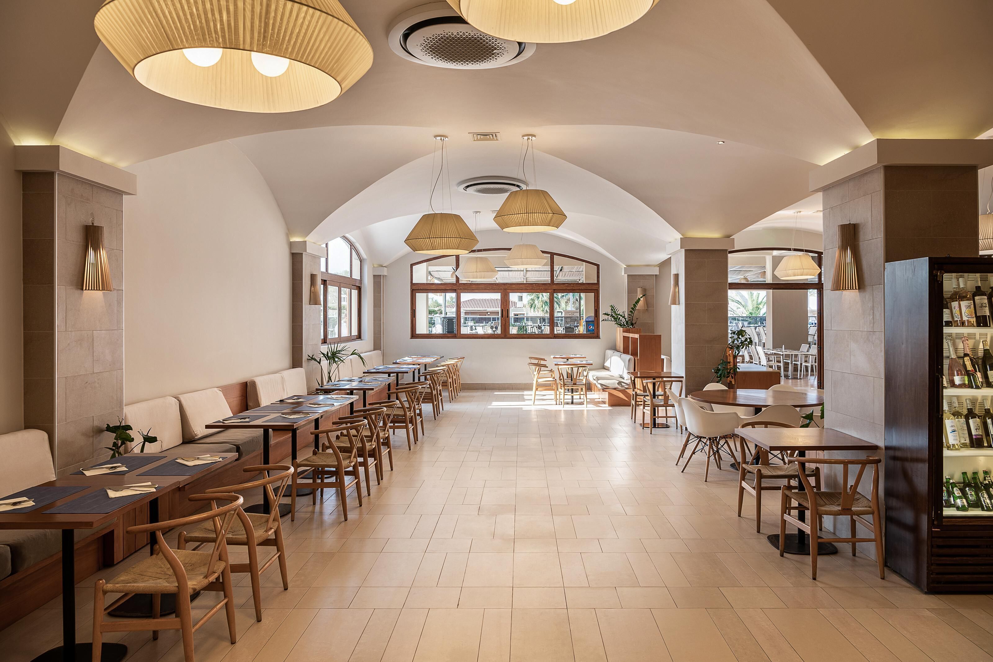 Un restaurante espacioso con techos altos, ventanas amplias y diversas opciones de asientos, incluyendo mesas y cabinas.