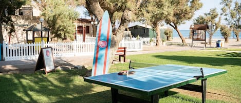 Una mesa de ping pong en un parque con una tabla de surf apoyada en un árbol.