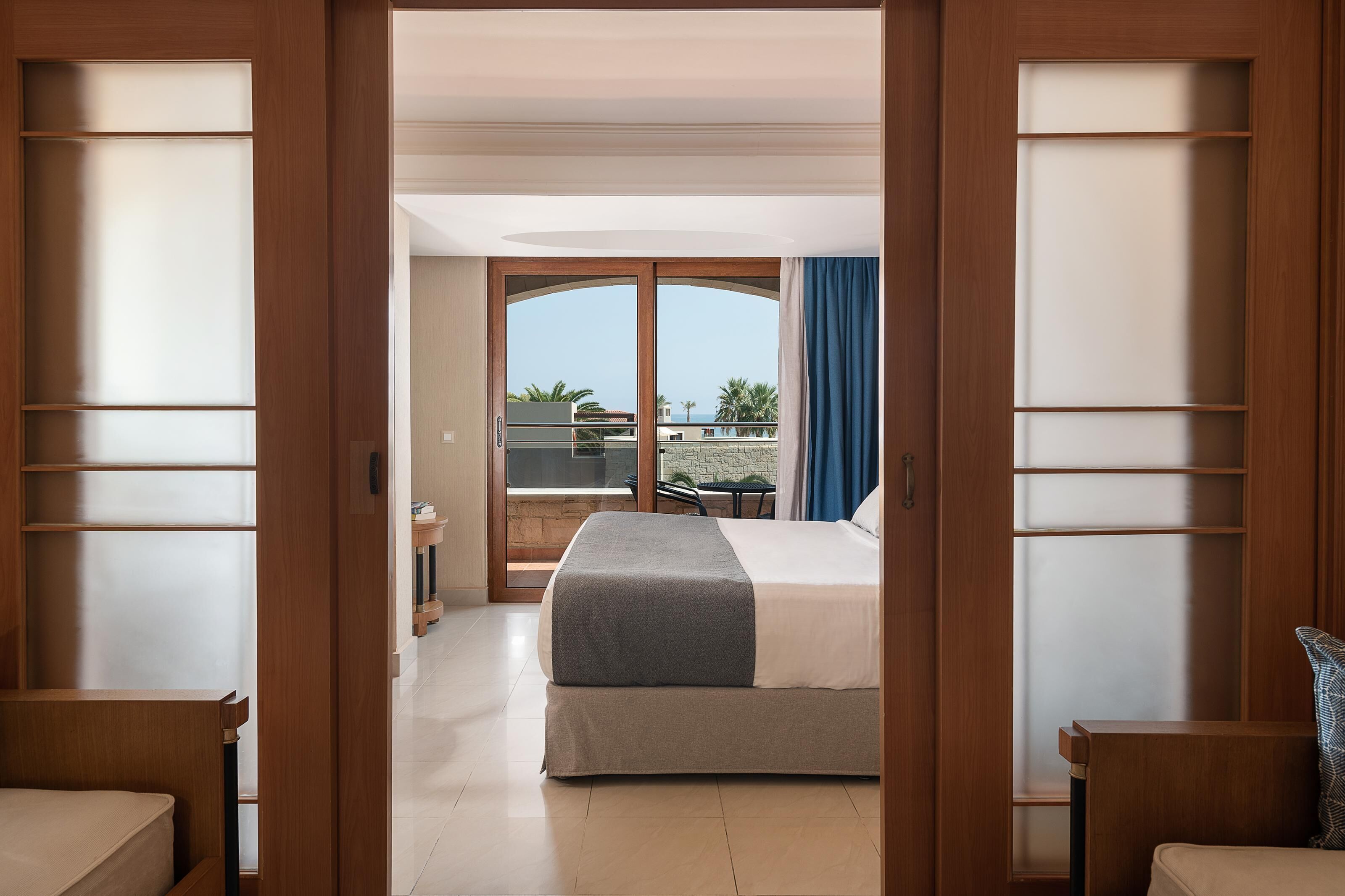A hotel room with a bed, a desk, and a balcony with a view of the sea.