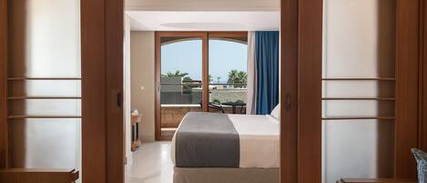 A hotel room with a bed, a desk, and a balcony with a view of the sea.