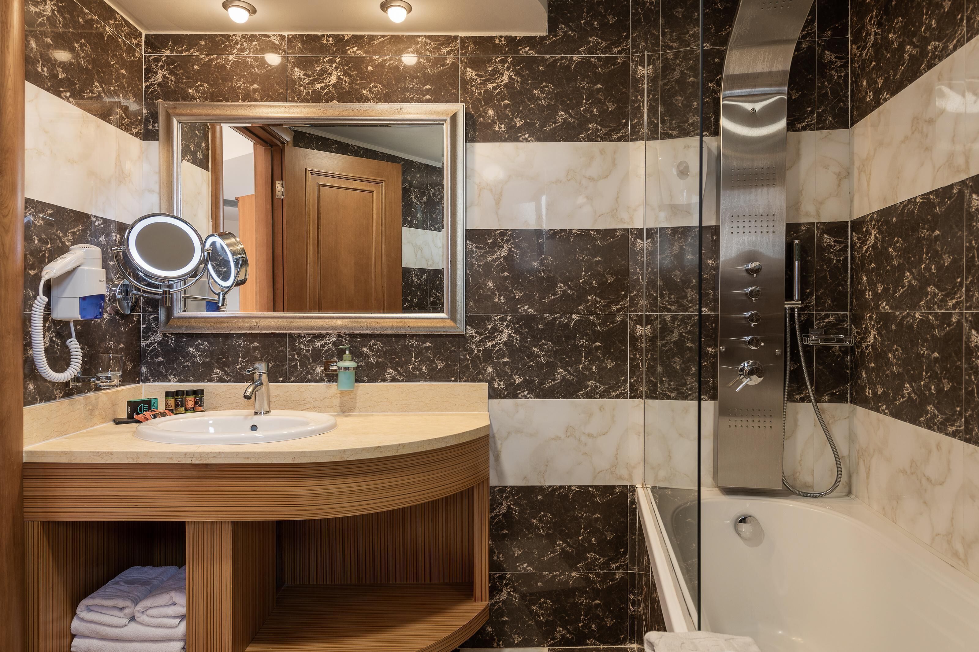 A modern bathroom with a vanity, a large mirror, a shower, and marble tiles.