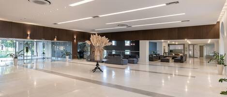 A spacious lobby with a modern design, featuring a large seating area, a decorative plant centerpiece, and a glass partition wall.