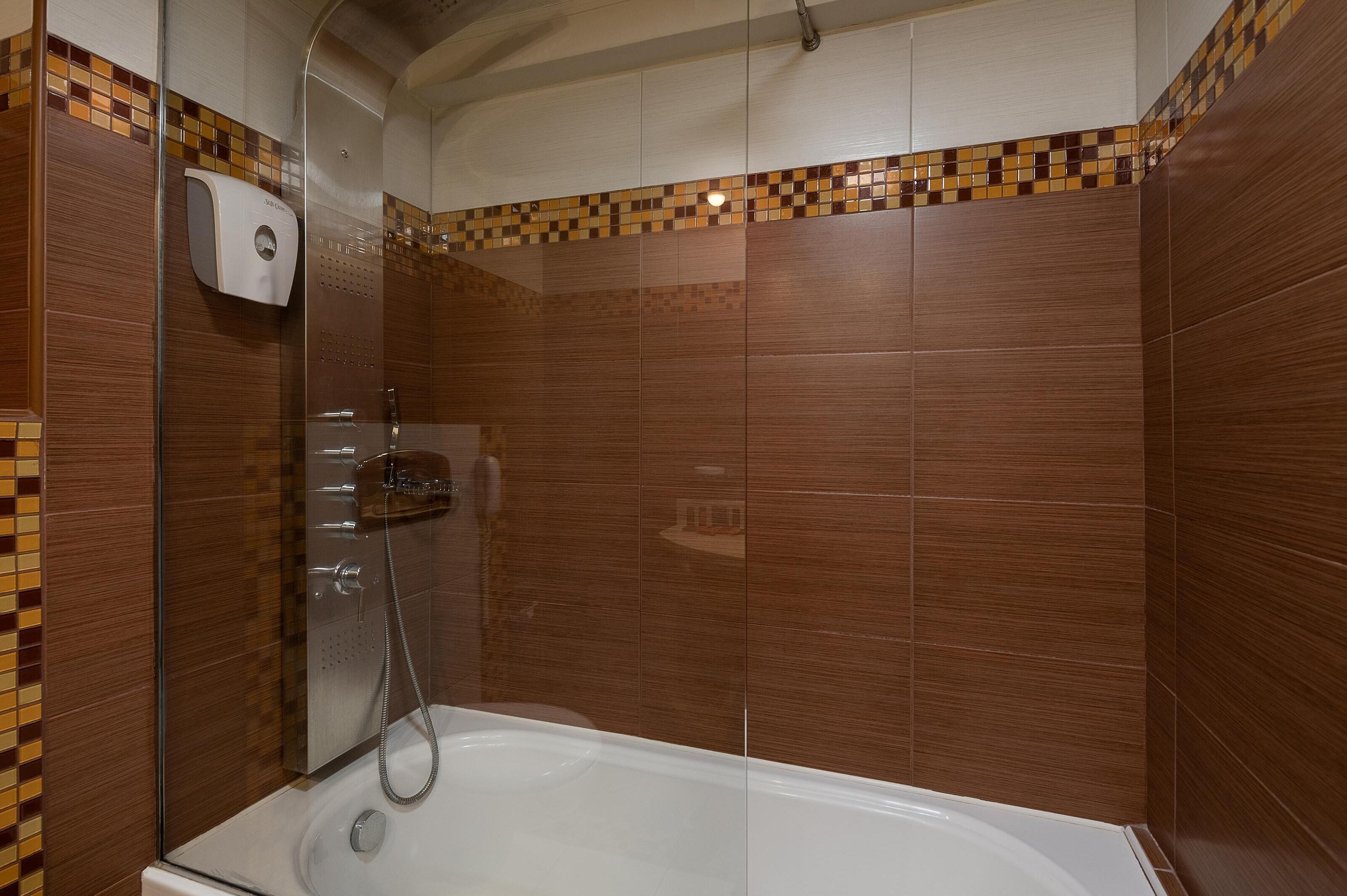 A modern bathroom with a glass-enclosed shower, a handheld showerhead, and a built-in toilet.