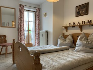 Ein Schlafzimmer mit Bett, Stuhl, Heizkörper, Fenster mit Vorhängen, Spiegel und Regal mit dem Schriftzug 'TRAUM'.