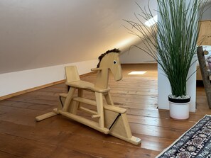 Ein hölzernes Schaukelpferd in einem Raum mit Holzboden, einer Topfpflanze und einem gemusterten Teppich.