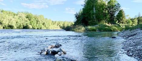 Ein Fluss mit Steinen und Bäumen im Hintergrund.