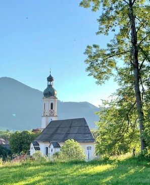 En kirke med et tårn og ur, omgivet af grønt og bakker.