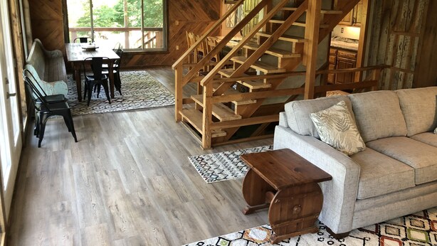 A spacious living area with a wooden staircase, a sofa, a dining table with chairs, and a large window providing natural light. - Lake front secluded house w/private boat/swim dock on 242 acre cattle ranch.  (Eagle Rock)
