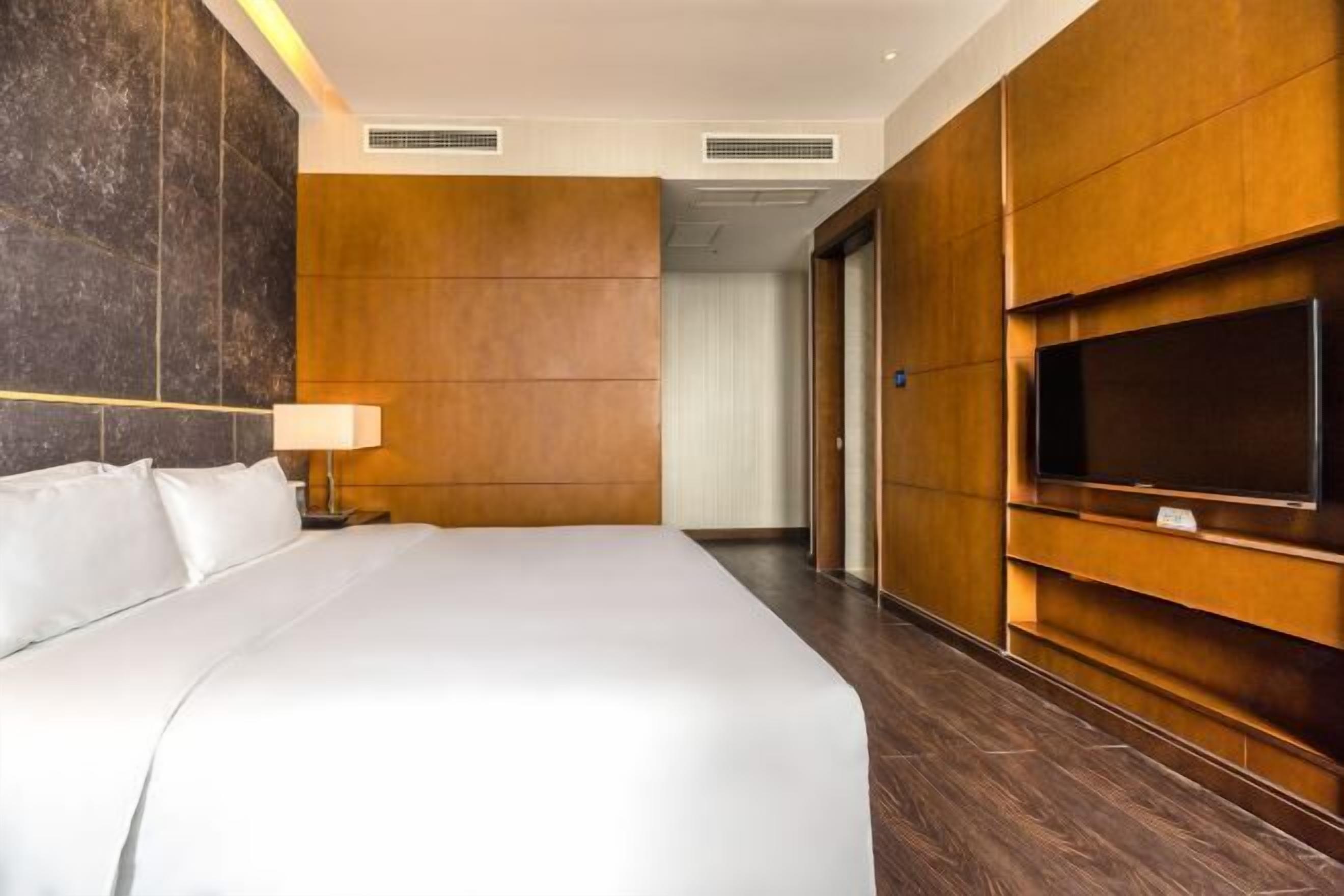 A hotel room with a large bed, a TV mounted on the wall, and a wooden panel design.