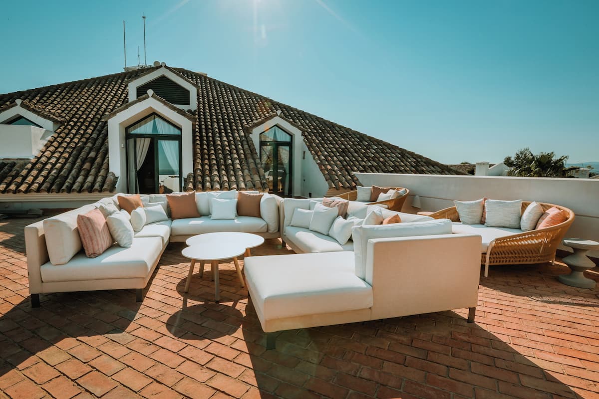 En tagterrasse med et hvidt loungesæt, et rundt bord og en fletstol. Terrassen har et fladt tag og en flisebelagt gulv.