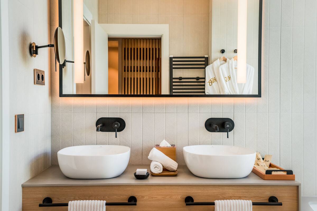 Et moderne badeværelse med to store, hvide håndvaske, et spejl og et trækommode.