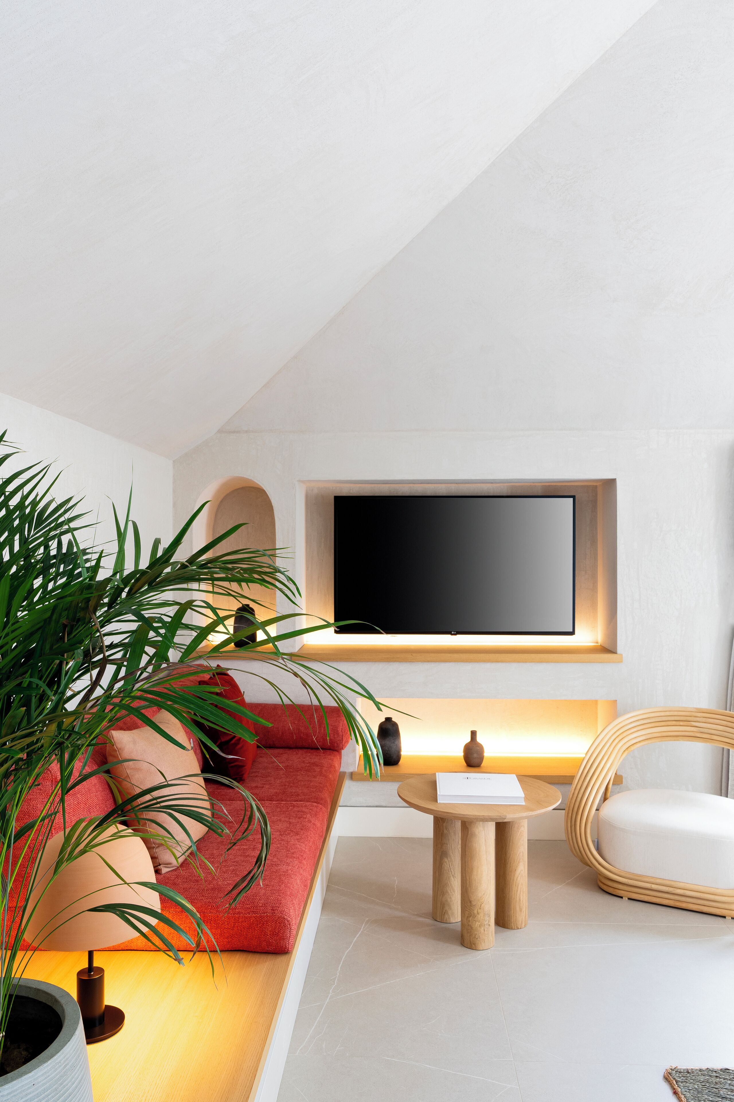 Ein modernes Wohnzimmer mit einem roten Sofa, einem runden Holztisch, einem großen Flachbildfernseher an der Wand und einem Blumentopf.