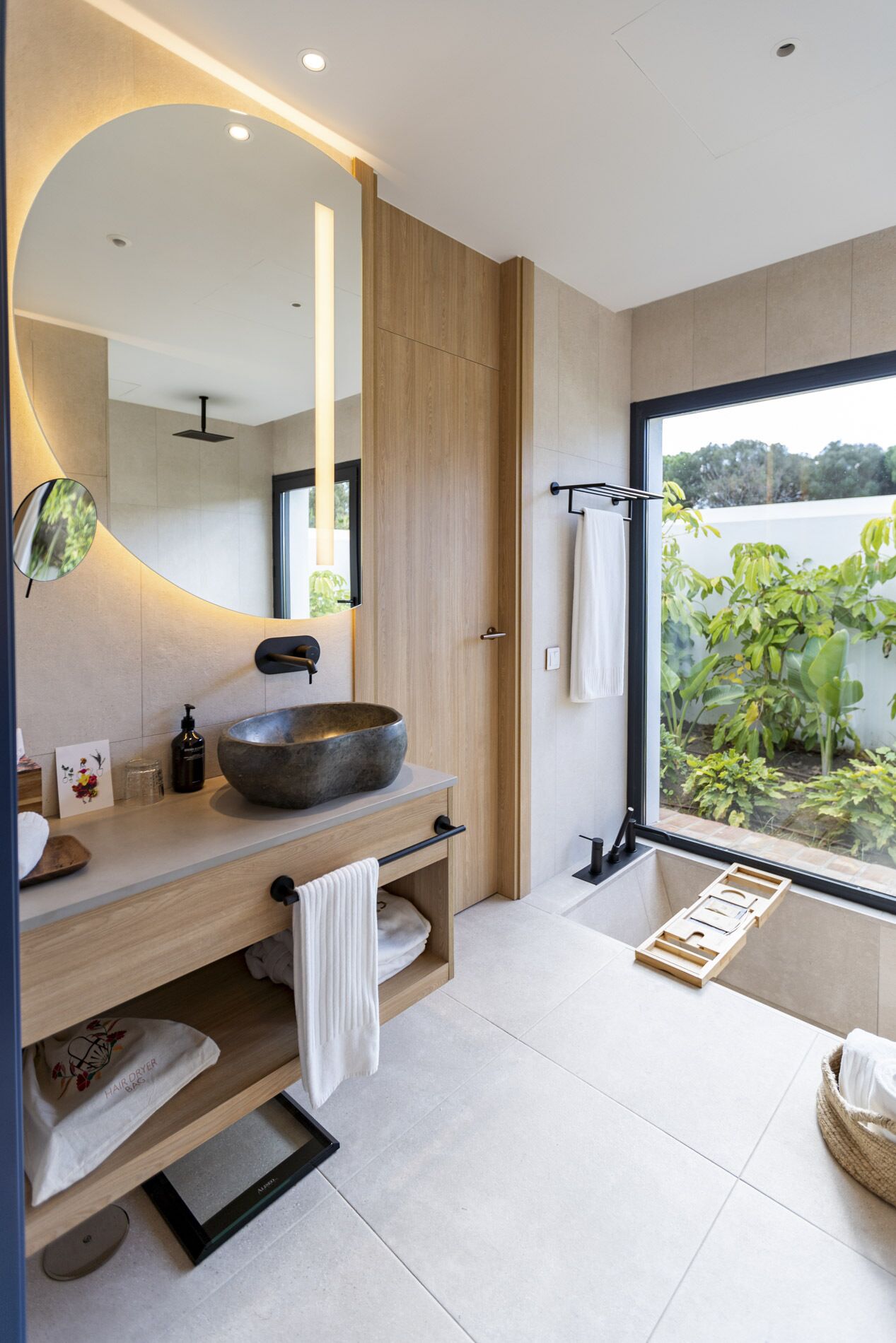 Une salle de bain moderne avec un grand lavabo rond, un miroir et une vue sur la verdure à l’extérieur.