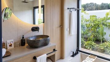 Un baño moderno con un lavamanos grande y redondo, un espejo y vistas a la vegetación exterior.