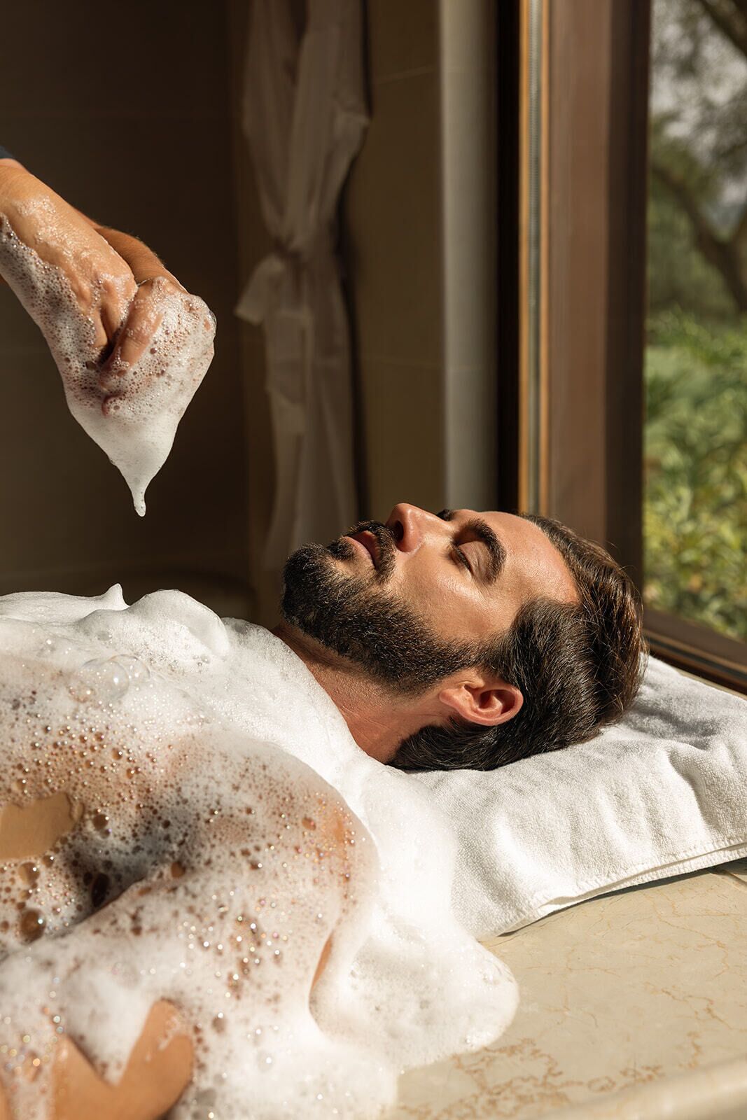 A person lying in a bathtub with bubbles, indicating a spa or bath service.