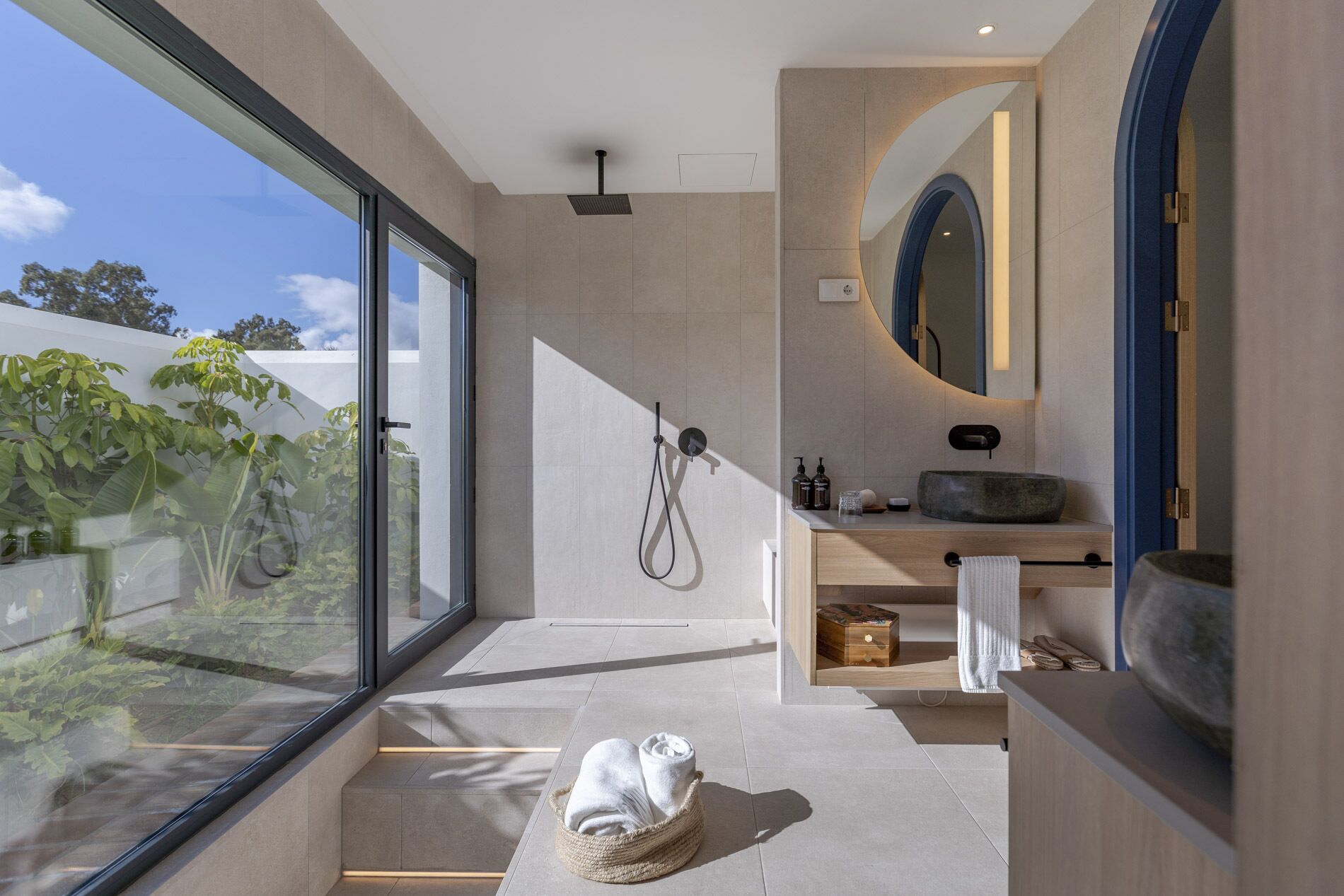 A modern bathroom with a large window, a shower, a sink with a round basin, and a mirror.