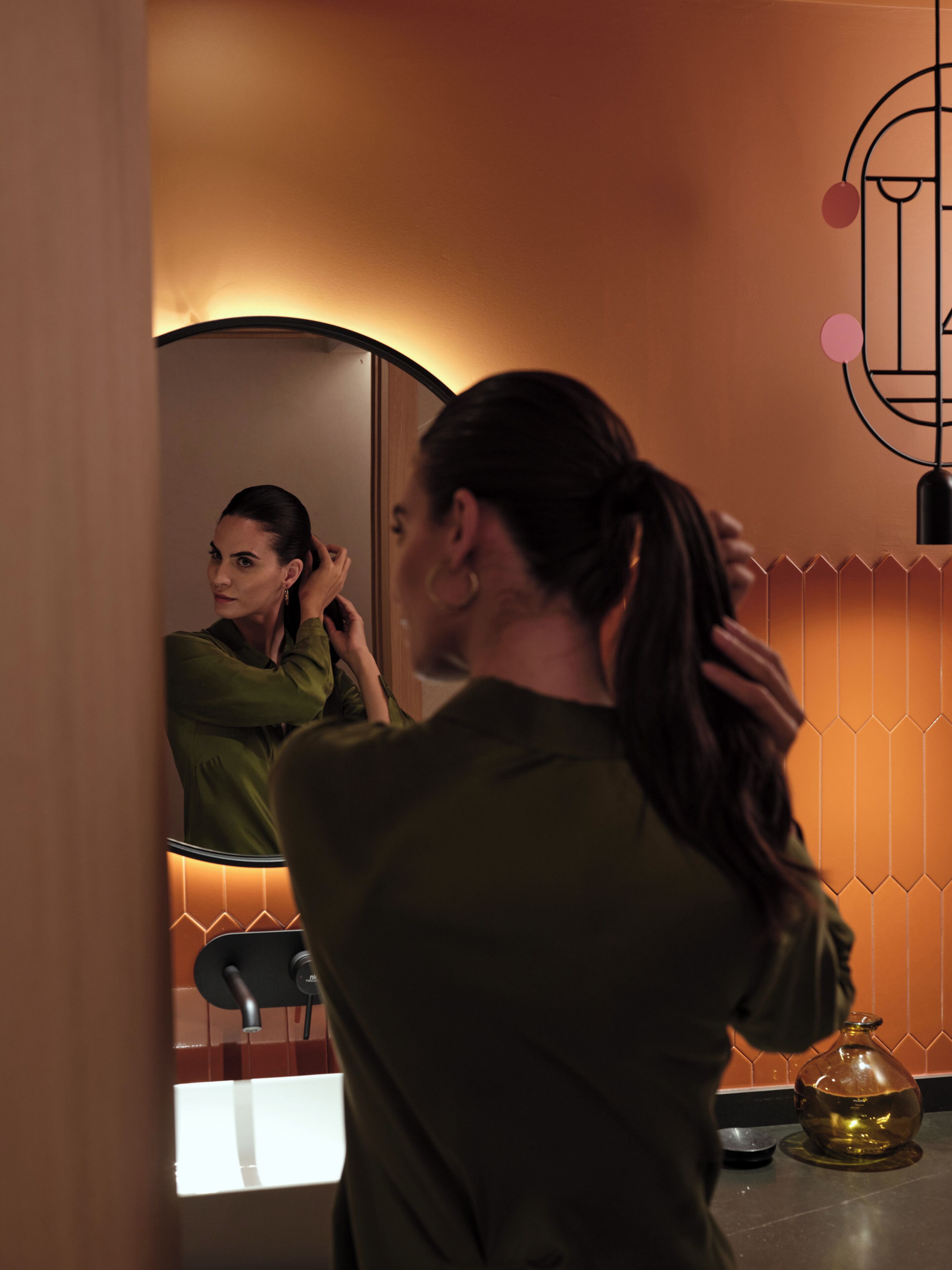 Un baño con espejo, lavabo y un jarrón decorativo en el mostrador.