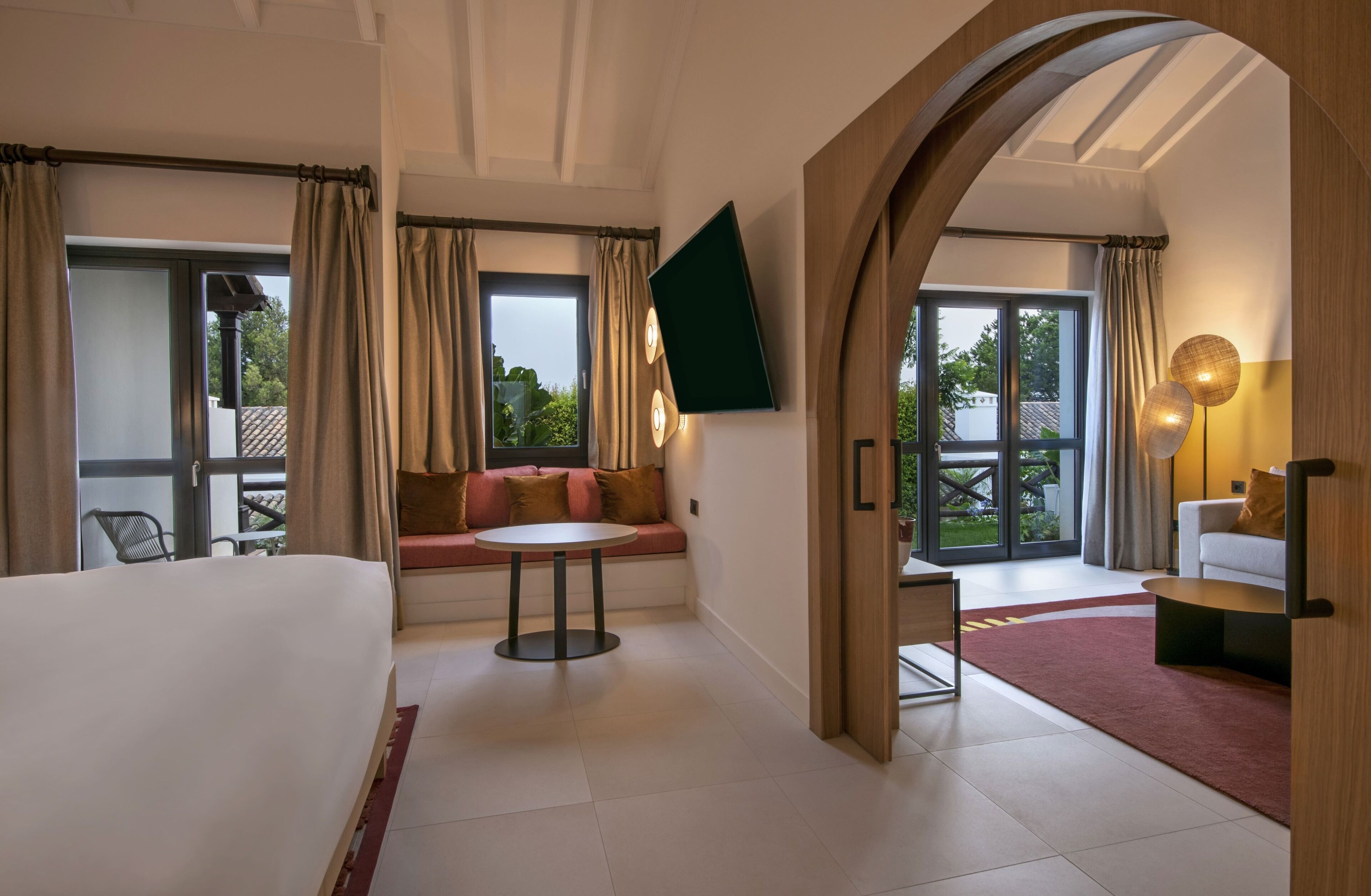 A hotel room with a bed, a sofa, a round table, and a TV mounted on the wall.