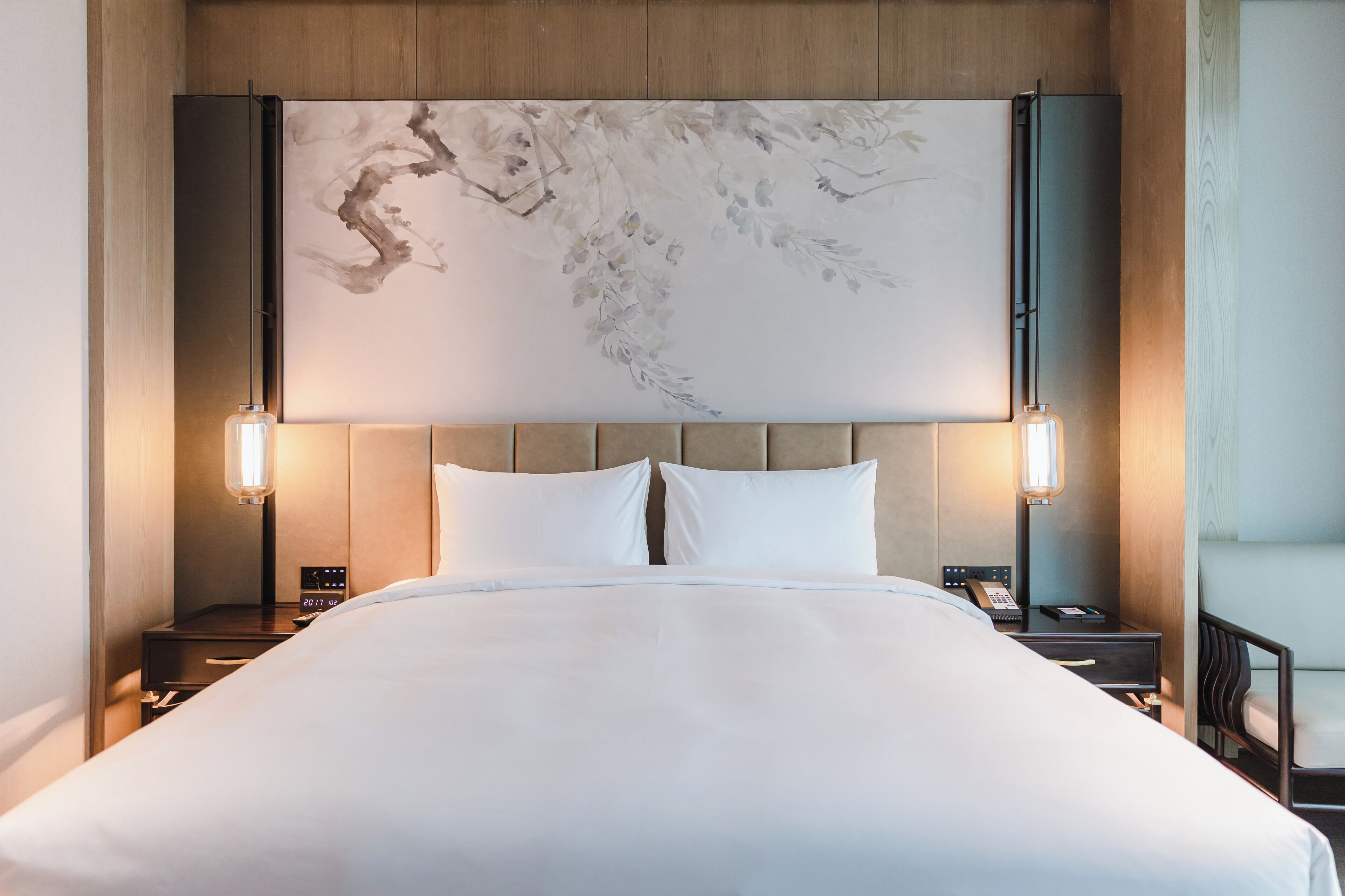 A hotel room with a large bed, two bedside tables, a wall-mounted artwork, and two wall-mounted lamps.
