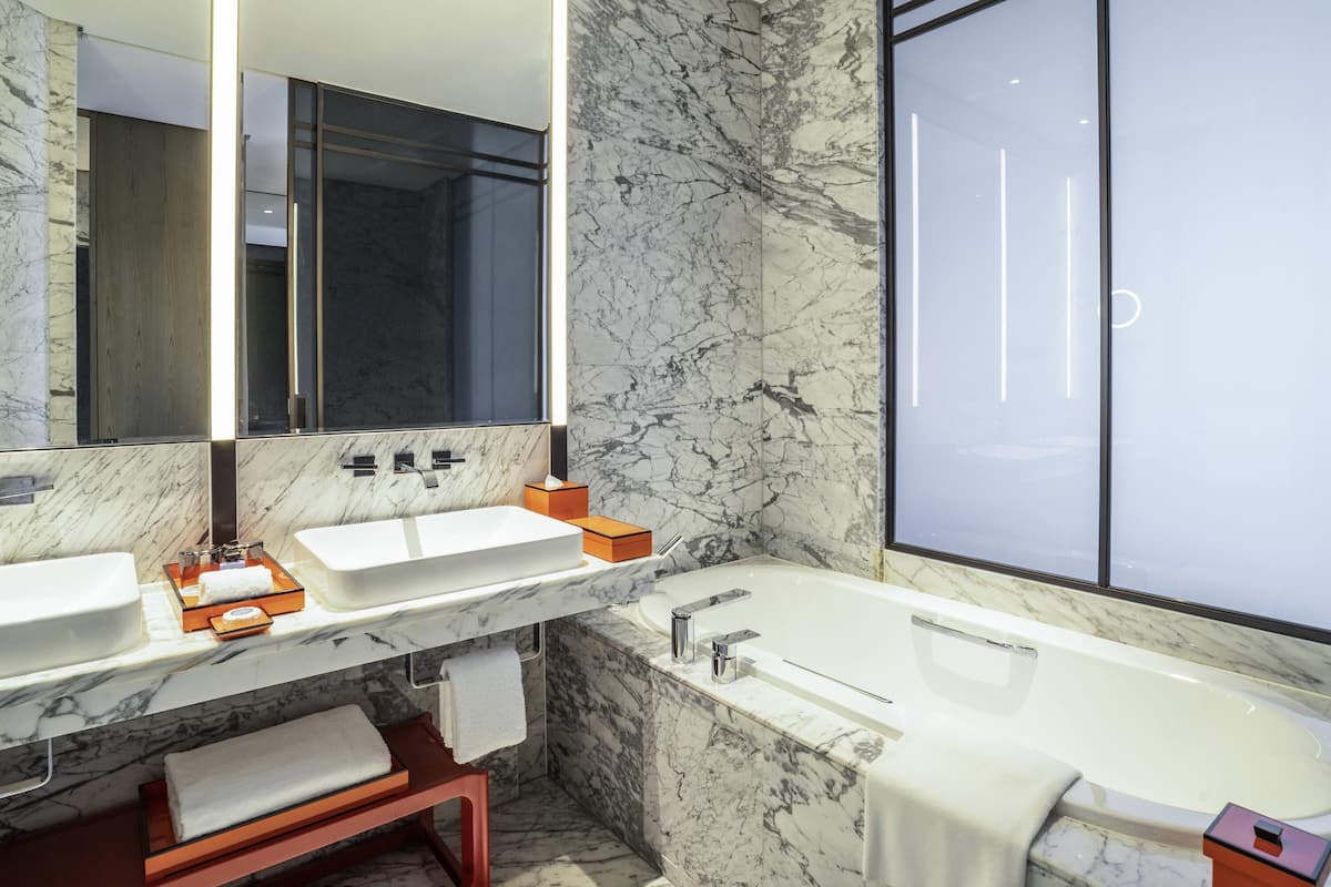 Une salle de bain moderne avec un grand miroir, deux lavabos, une baignoire et des murs en marbre.