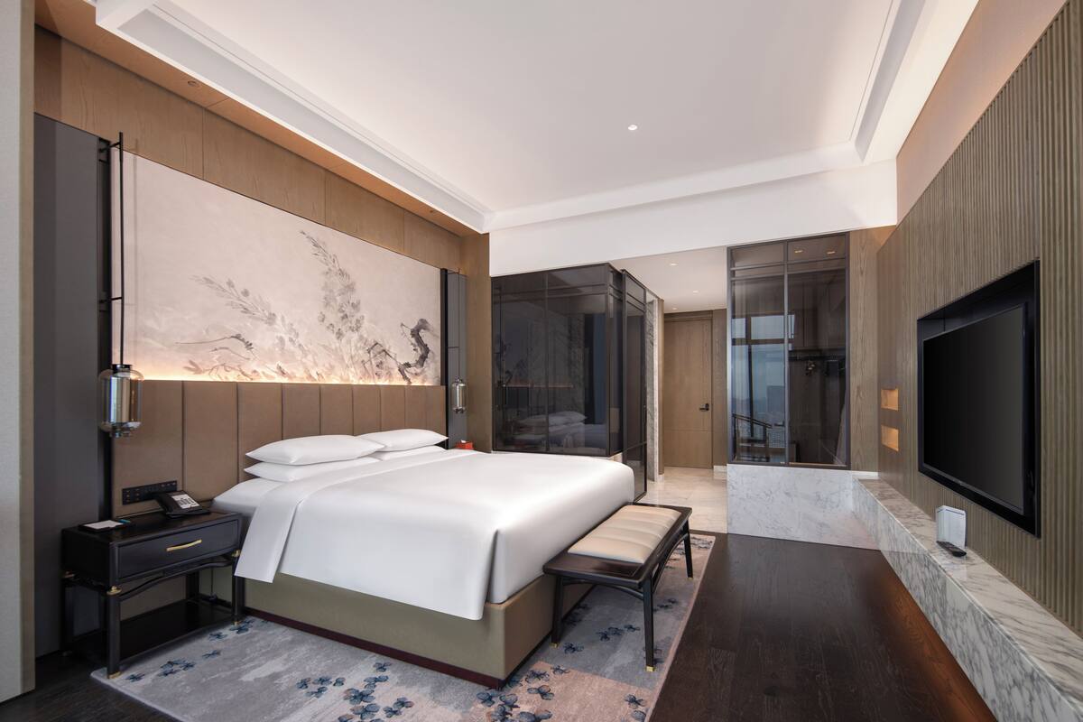 Een moderne hotelkamer met een groot bed, nachtkastje en een flatscreen televisie aan de muur.