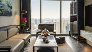 A modern living room with a sofa, a coffee table with a teapot, a chair, a large window with a city view, and a TV on the wall. - Sofitel Hangzhou Yingguan Hotel (Hangzhou)