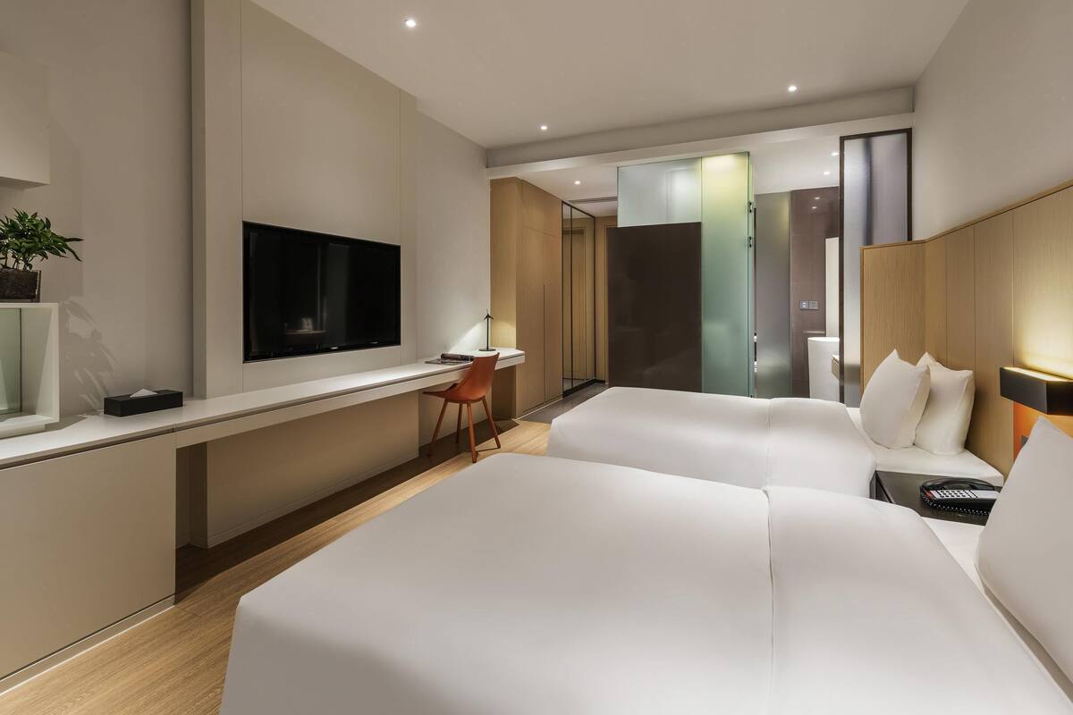 Una habitación de hotel moderna con una cama grande, un escritorio con silla, un televisor y una mesita de noche con lámpara.