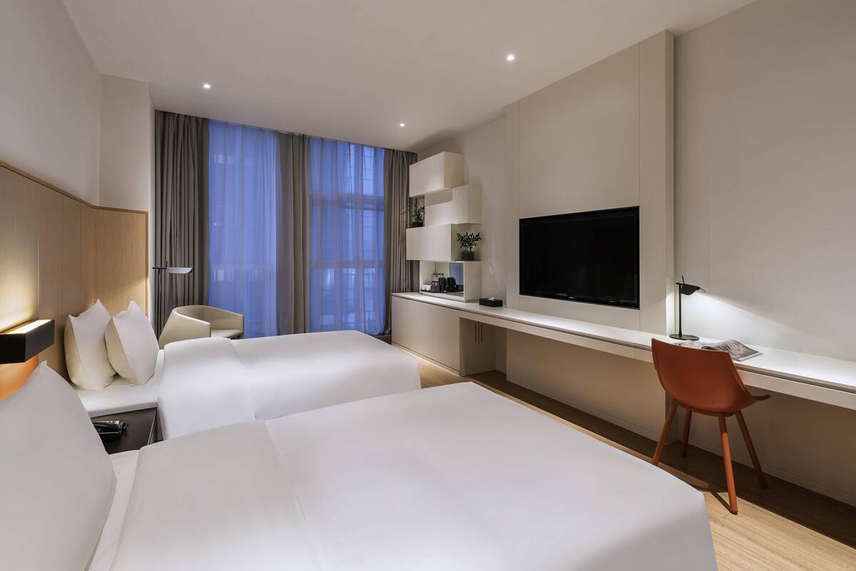 Una habitación de hotel moderna con dos camas, un escritorio, un televisor y una silla.