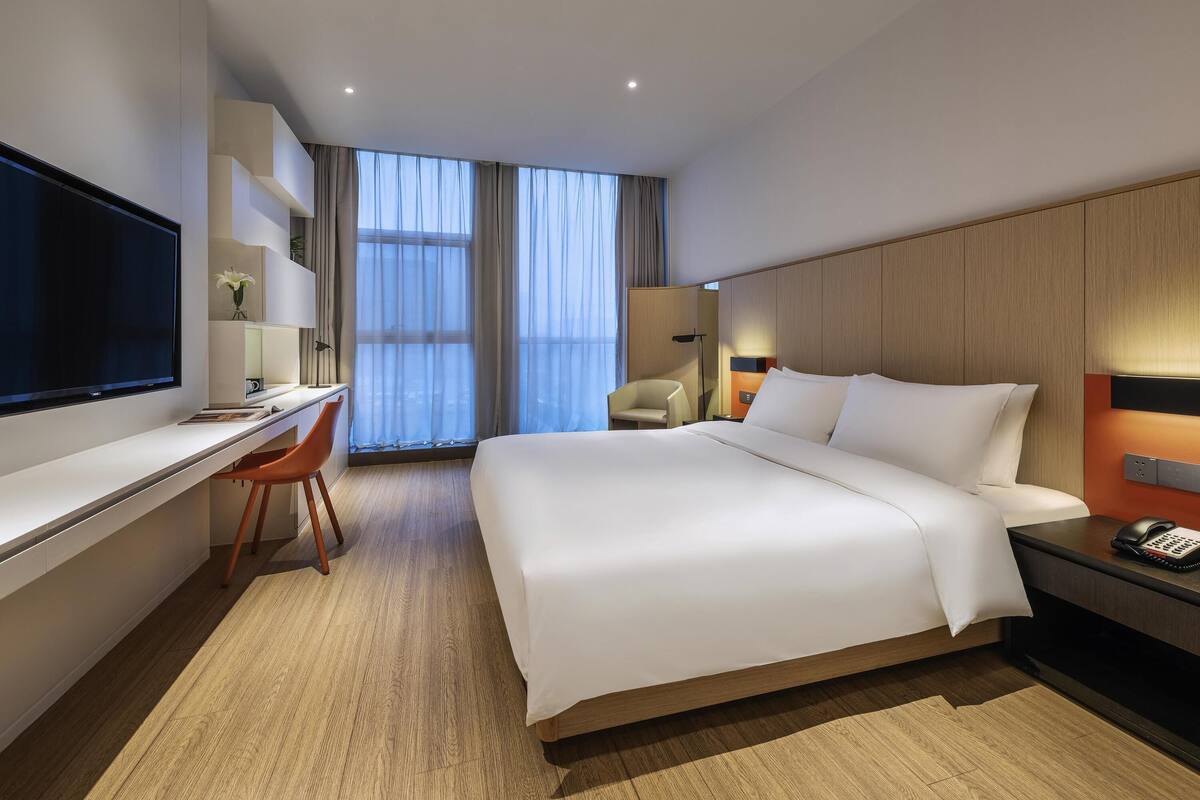 Una habitación de hotel moderna con una cama grande, un escritorio con silla, un televisor y una mesita de noche con teléfono.